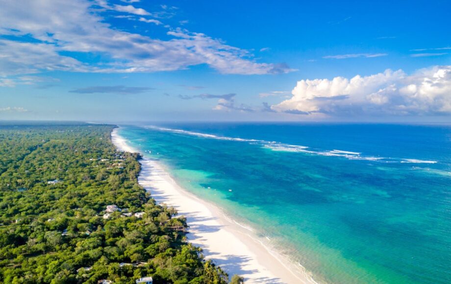 Hvit sandstrqand på Diani Beach Kenya med trær på den ene siden og turkis hav på den andre