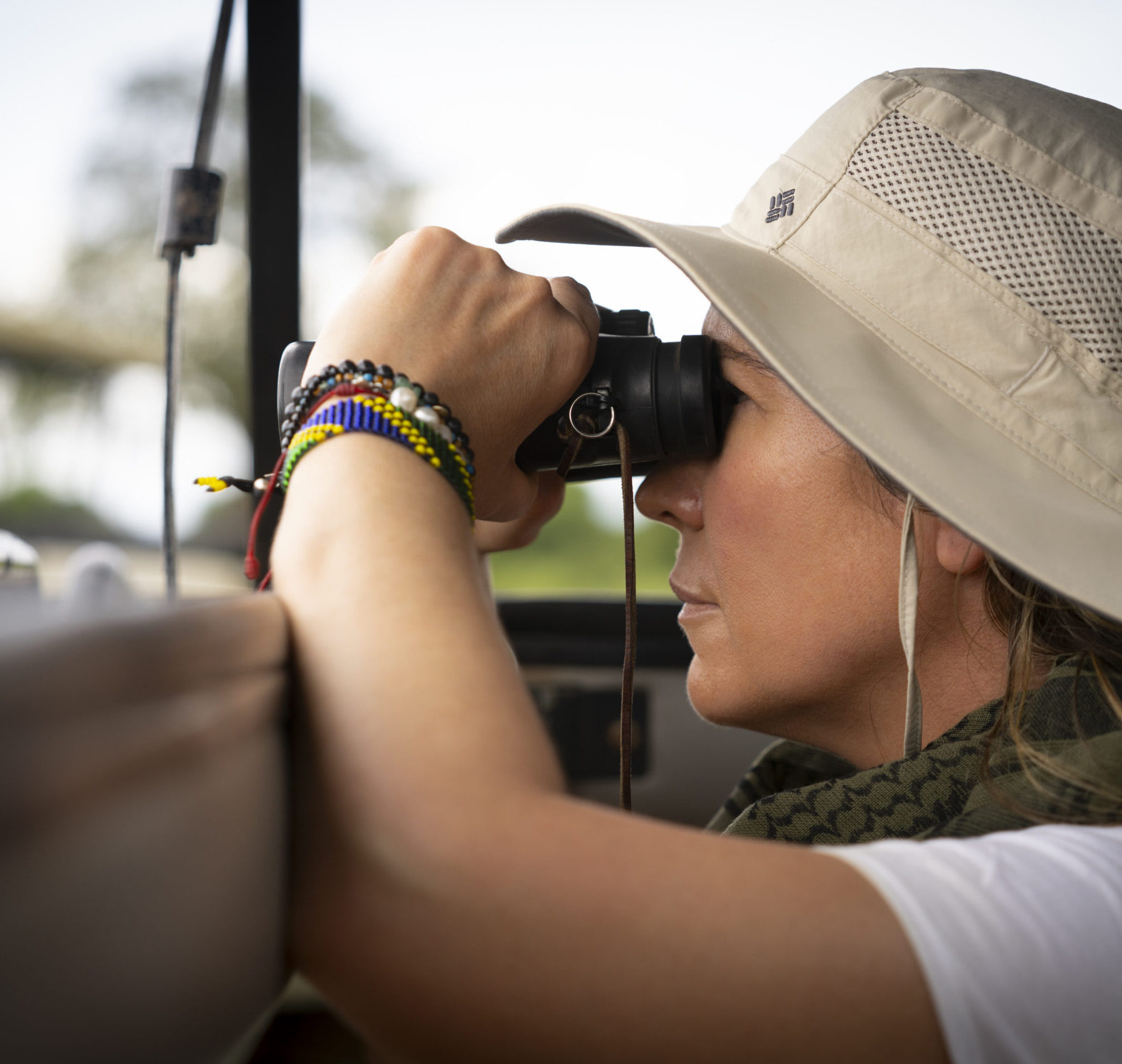 Kvinne med hatt og kikkert ser ut fra en bil i Serengeti
