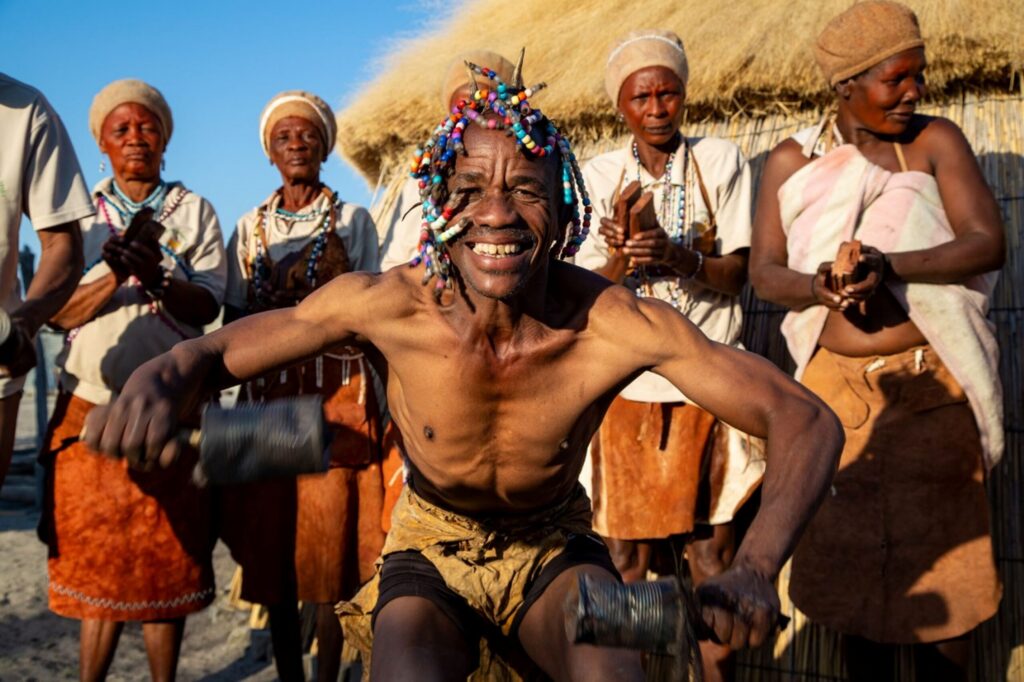Mennesker fra Khwai-landsbyen står i en halvsirkel med en mann som danser og smiler foran