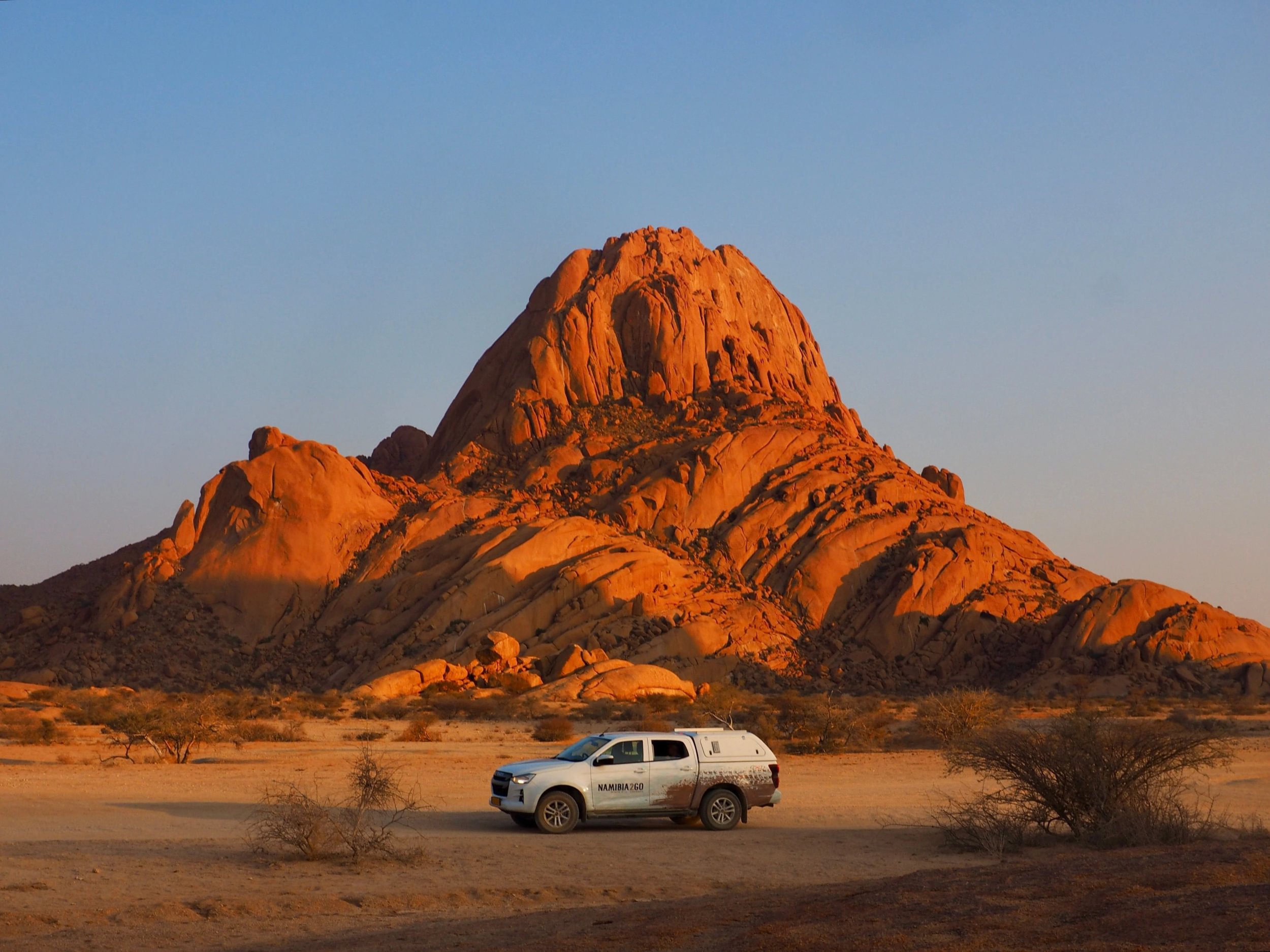 Safarikjøretøy parkert under Spitzkoppe i solnedgang