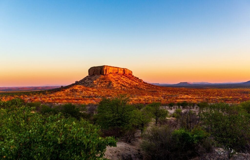 Waterberg Plateau Namibia med solnedgang bak fjellet og trær i forgrunnen